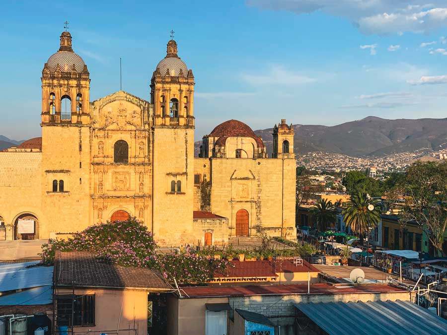 Twin-towered colonial church in golden stone with hills behind it