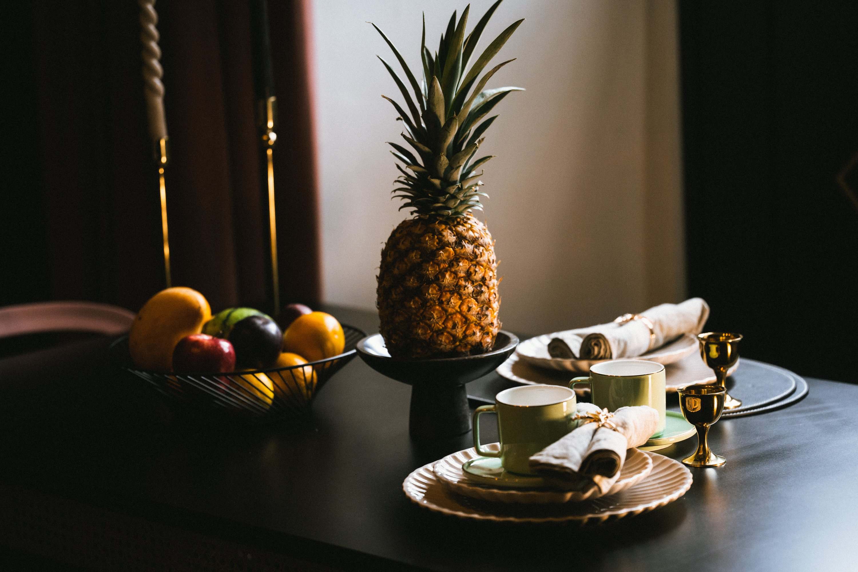 Welcome table at a HOLT hotel set with a pineapple, a fruit bowl, cups, gold goblets and linen napkins