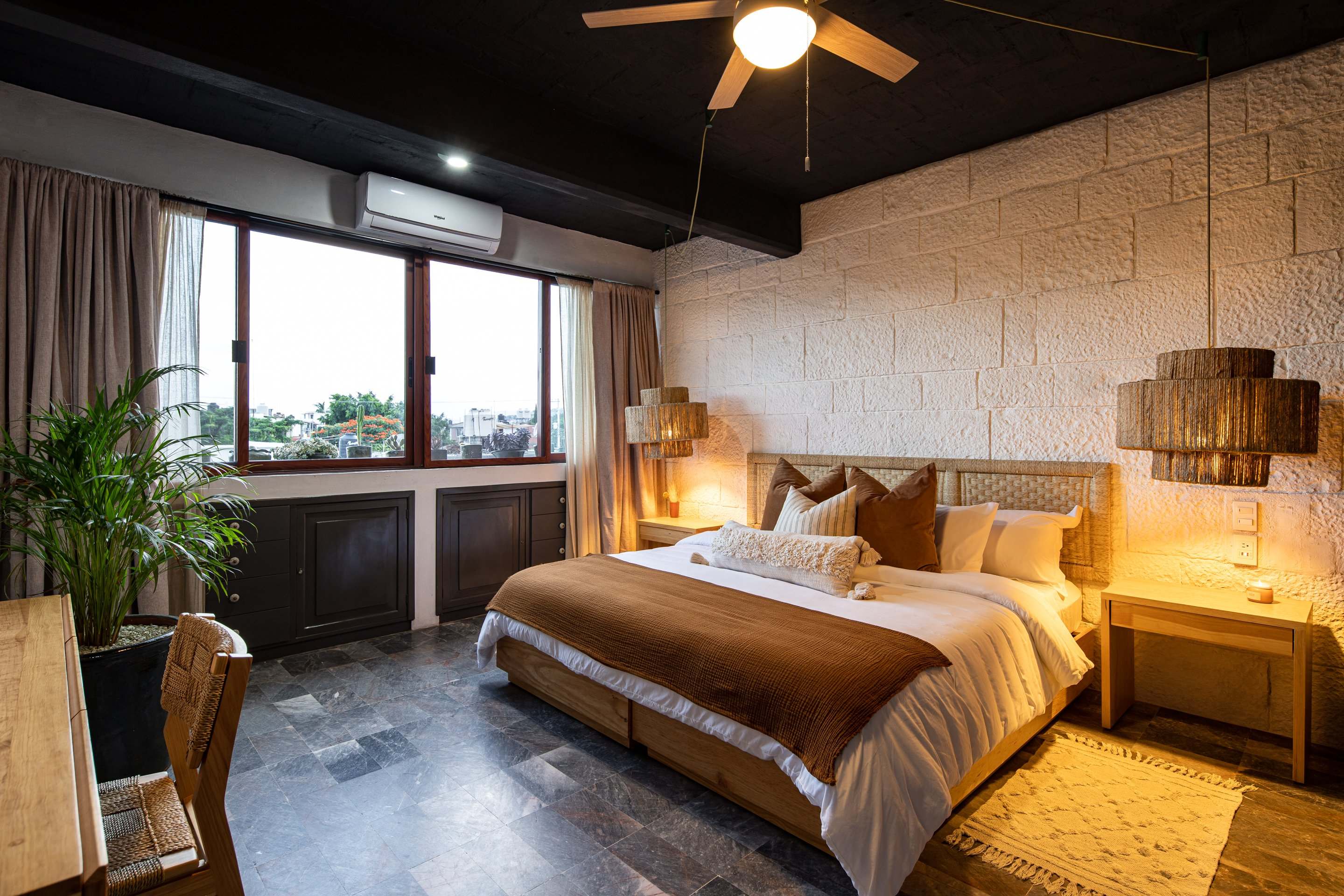 Bedroom at Villa Noria, a HOLT property in Oaxaca, with stone walls, woven pendant lamps and a window over the city